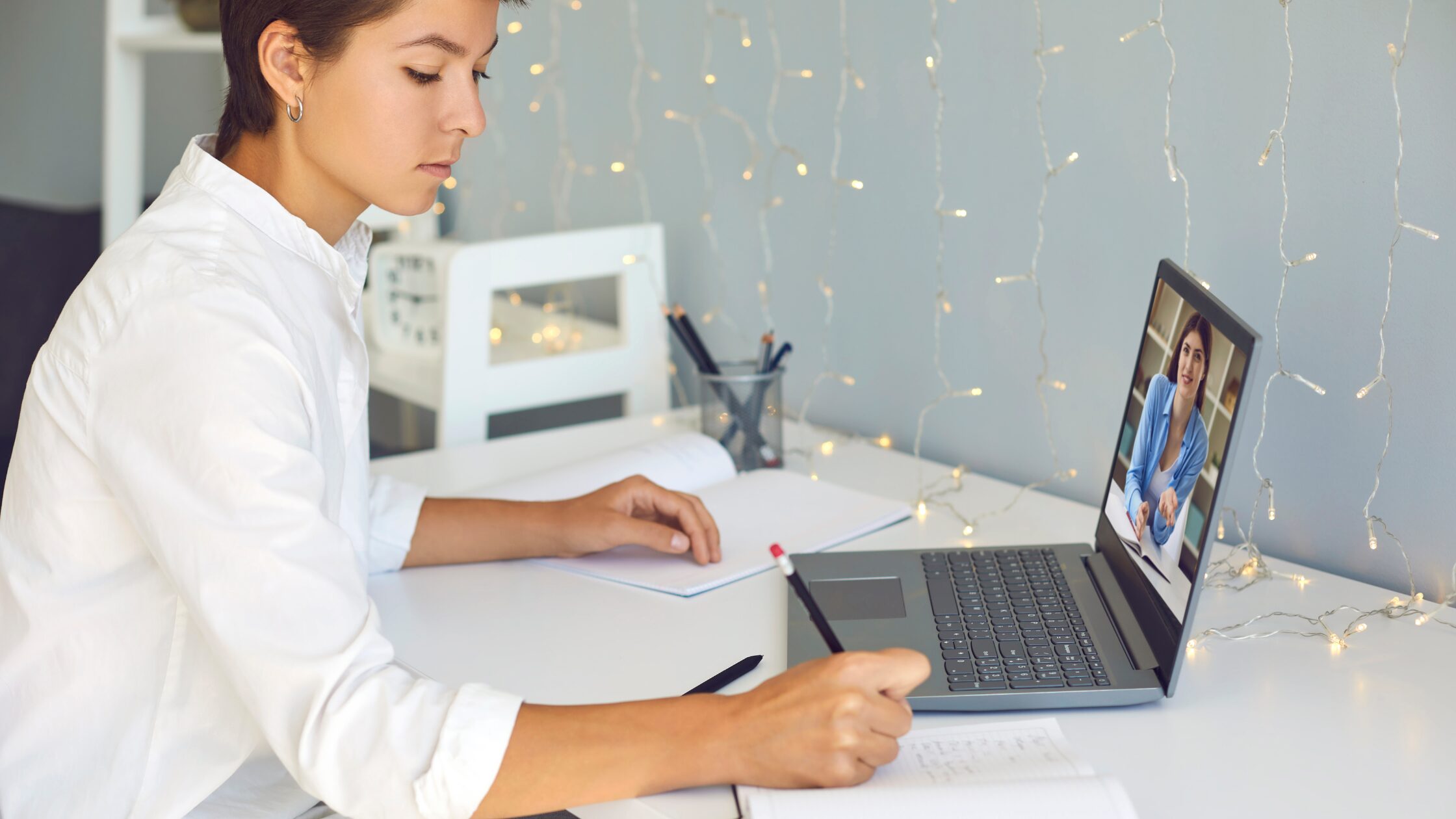 Woman sat a desk on a video call on a laptop, taking notes in a notebook
