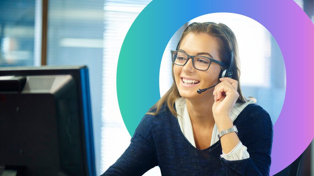 Woman smiling sat a desk, with headphones on for a work call