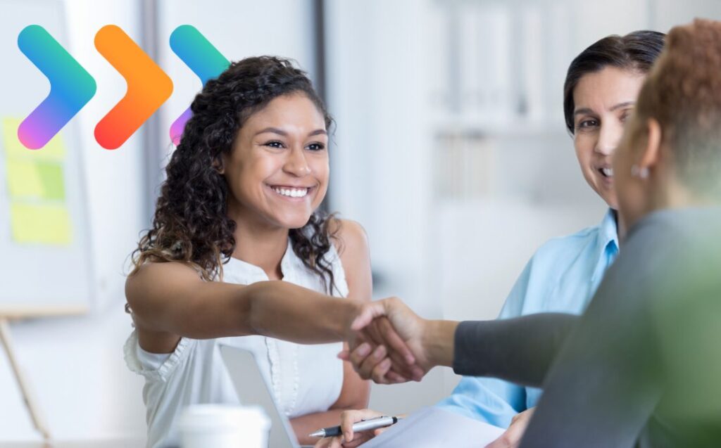 Woman smiling while reaching across a desk to shake hands with a colleague