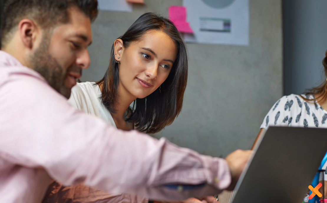 Two colleagues looking at a laptop together, one pointing at the screen while the other watches