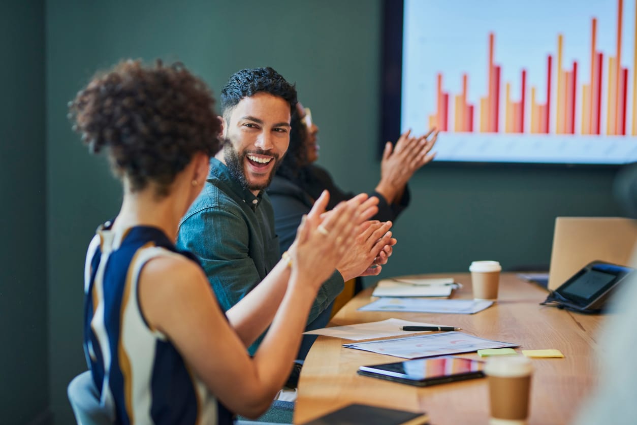 Group of business professionals clapping and smiling during a meeting in the boardroom.