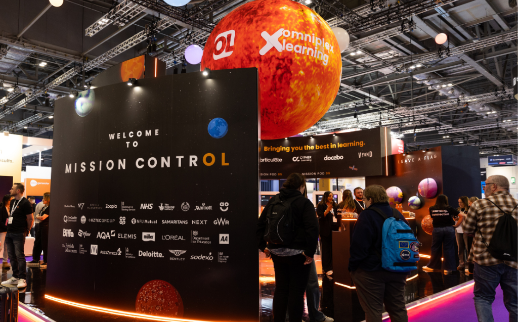 A photo of the Omniplex Learning stand at Learning Technologies - featuring a big orange sun hovering from the ceiling and people visiting the stand.